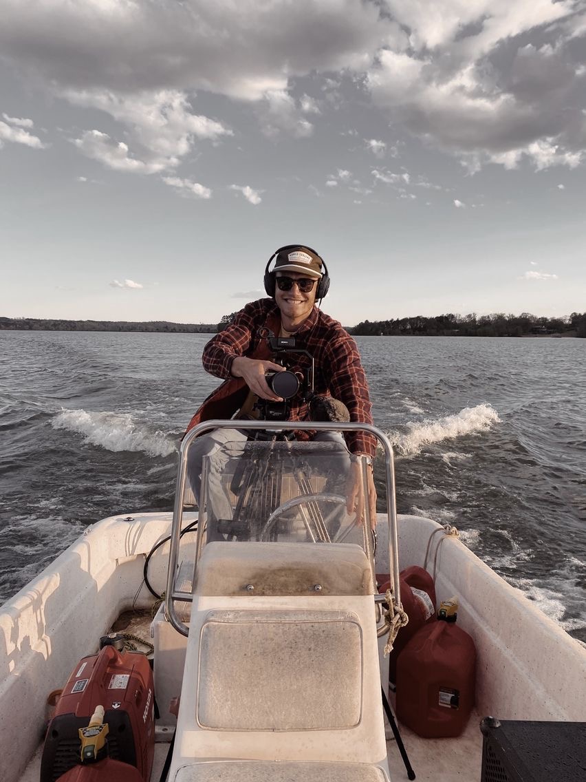 Jacob Smock driving a motorboat while operating a camera.